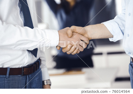 Two businessmen are shaking hands in office, close-up. Happy and excited business woman stands with raising hands at the background. Business people concept 76014564