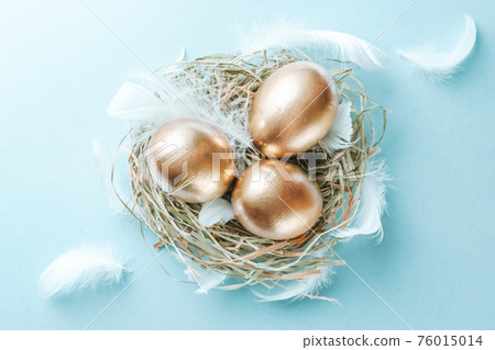 Easter Golden eggs in basket with white feathers on pastel blue background in Happy Easter decoration. Spring holiday flat lay concept. Easter Golden eggs in basket with white feathers on pastel blue background in Happy Easter decoration. Spring holiday flat lay concept. 76015014