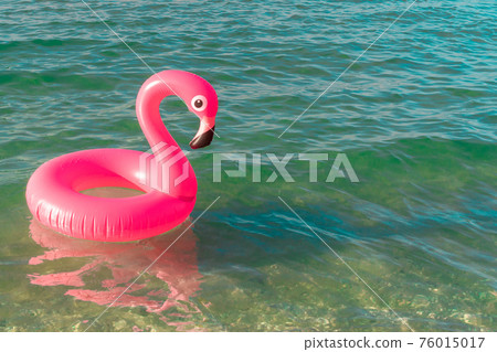 Sea background. Pink inflatable flamingo in blue ocean water for sea summer beach background. Luxury lifestyle travel. Sea background. Pink inflatable flamingo in blue ocean water for sea summer beach background. Luxury lifestyle travel. 76015017