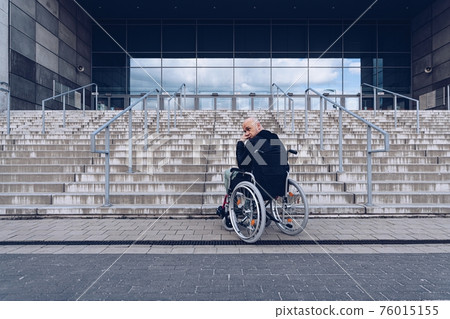 Disabled man in a wheelchair waiting at the bottom of steps. Disabled man in a wheelchair waiting at the bottom of steps. 76015155
