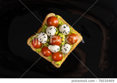 A cheese and tomato sandwich sits in a black plate on a wooden background A cheese and tomato sandwich sits in a black plate on a wooden background 76016469
