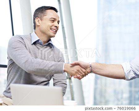 caucasian business executive smiling and shaking hand with another person in office. 76019066