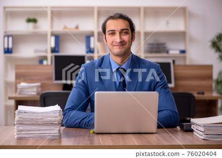 Young male employee and a lot of work in the office Young male employee and a lot of work in the office 76020404