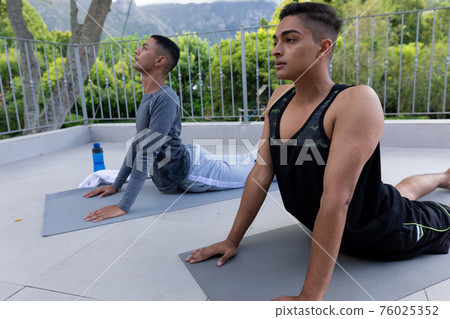 Diverse gay male couple practicing yoga on balcony 76025352