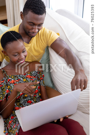 African american couple sitting on sofa using laptop computer and smiling 76025393
