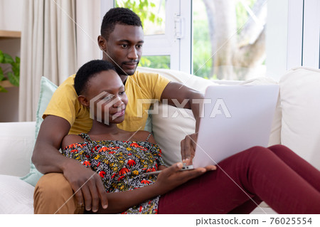 African american couple sitting on sofa using laptop computer and smiling African american couple sitting on sofa using laptop computer and smiling 76025554