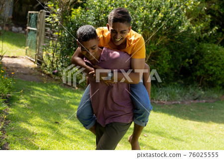 Diverse gay male couple spending time in garden embracing and smiling Diverse gay male couple spending time in garden embracing and smiling 76025555