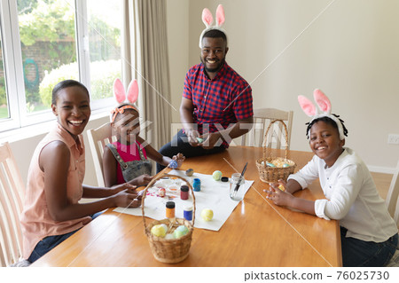 Happy african american parents with son and daughter wearing bunny ears painting easter eggs Happy african american parents with son and daughter wearing bunny ears painting easter eggs 76025730