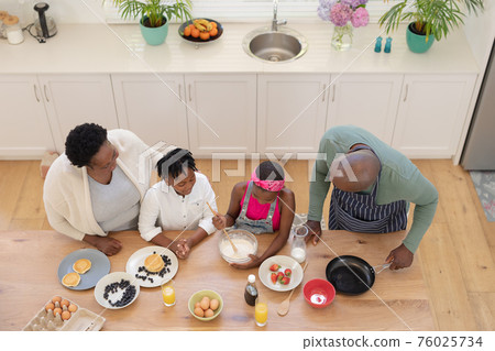 High angle view of african american grandparents teaching grandchildren cooking in the kitchen High angle view of african american grandparents teaching grandchildren cooking in the kitchen 76025734