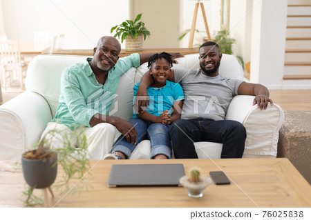 Portrait of senior african american fon couch smiling with adult son and grandson embracing 76025838