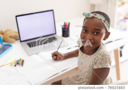 Portrait of african american girl at desk using laptop with copy space for online school lesson Portrait of african american girl at desk using laptop with copy space for online school lesson 76025883