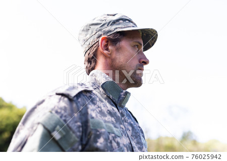 Caucasian male soldier wearing camo fatigues and cap standing outdoors looking away Caucasian male soldier wearing camo fatigues and cap standing outdoors looking away 76025942