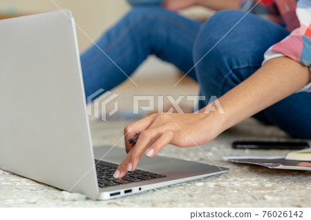 Mixed race woman sitting on the floor working from home using laptop 76026142