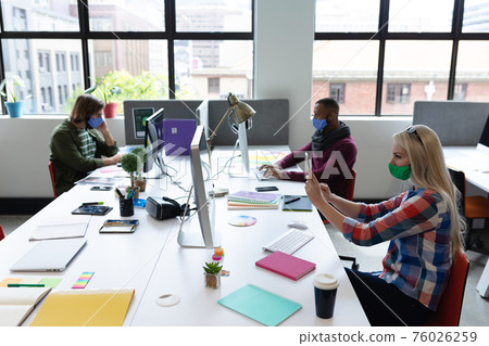 Diverse group of business people wearing face masks in creative office Diverse group of business people wearing face masks in creative office 76026259