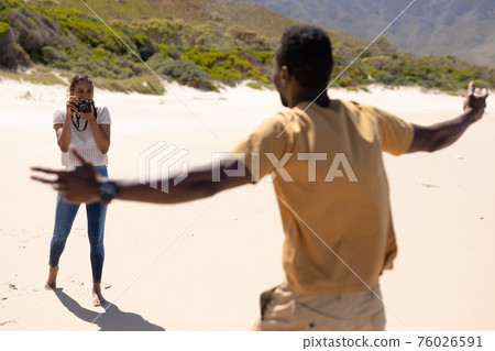 African american couple taking photos with camera on a beach by the sea 76026591
