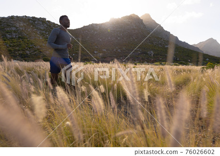 Fit african american man in sportswear running through tall grass 76026602