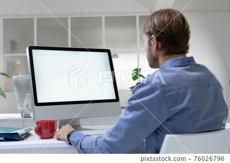 Rear view of caucasian businessman sitting at desk making video call using desktop computer 76026796