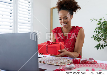 African american woman holding gift box on videocall on laptop at home 76026852