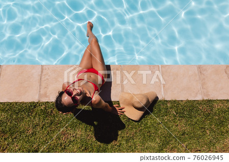 Mixed race woman sunbathing by pool on a sunny day Mixed race woman sunbathing by pool on a sunny day 76026945