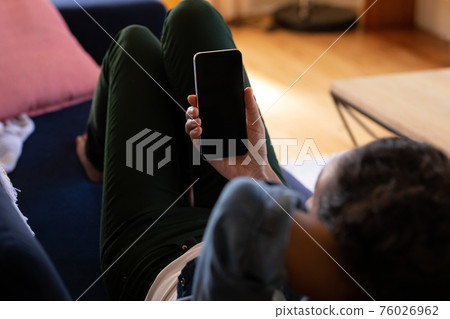Caucasian woman using smartphone lying on sofa at home 76026962