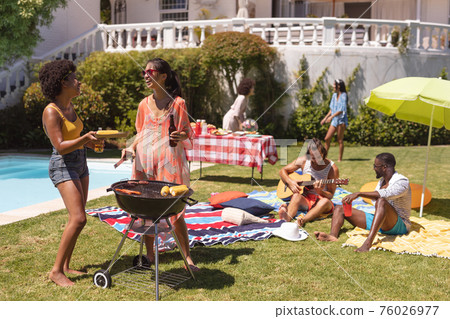 Diverse group of friends having barbecue and talking at a pool party 76026977