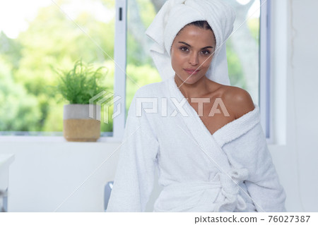 Caucasian woman wearing bathrobe sitting on bathtub edge looking at camera and smiling Caucasian woman wearing bathrobe sitting on bathtub edge looking at camera and smiling 76027387