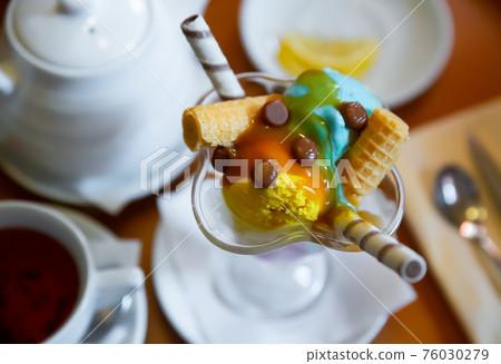 Dessert of two scoops of ice cream, waffle and chocolate candy 76030279