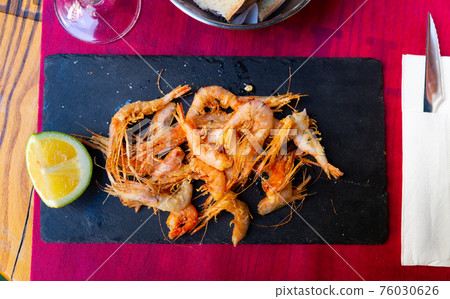 Tasty fried shrimps served with lemon in black plate 76030626