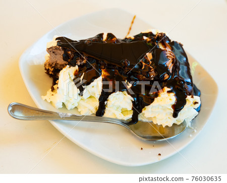 Slice of tasty chocolate cake served on white plate with whipped cream Slice of tasty chocolate cake served on white plate with whipped cream 76030635