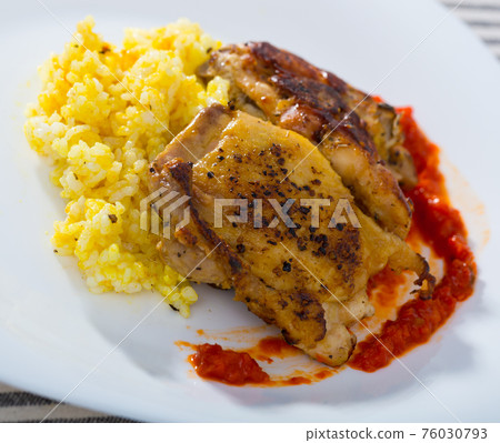 Tasty rice with chicken thighs and red sauce at plate on table Tasty rice with chicken thighs and red sauce at plate on table 76030793