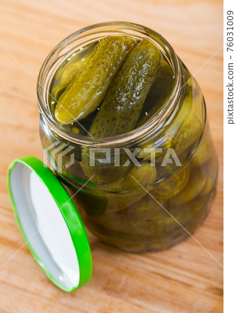 Opened glass jar with pickled cucumbers on wooden background 76031009