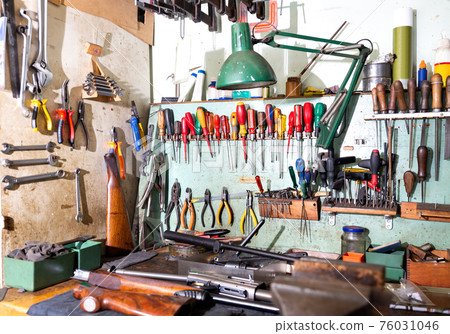 Workplace of gunsmith in weapons workshop with tools and disassembled shotgun Workplace of gunsmith in weapons workshop with tools and disassembled shotgun 76031046