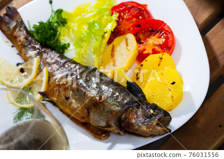 Baked whole trout with potatoes, tomatoes and greens on plate, glass of wine Baked whole trout with potatoes, tomatoes and greens on plate, glass of wine 76031556