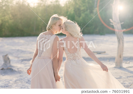 Two brides women in white dress with blonde hair hugging each other Two brides women in white dress with blonde hair hugging each other 76031991