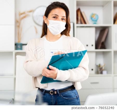 Woman in protective mask with blue folder of documents stands Woman in protective mask with blue folder of documents stands 76032240