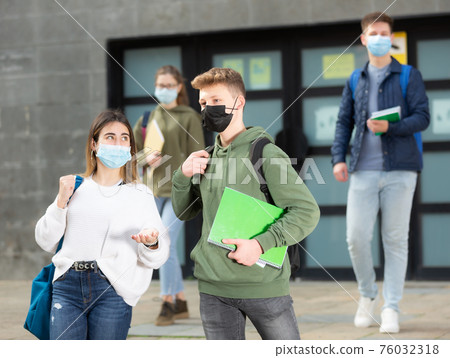 Young girl and guy in protective masks walk along street holding hands 76032318