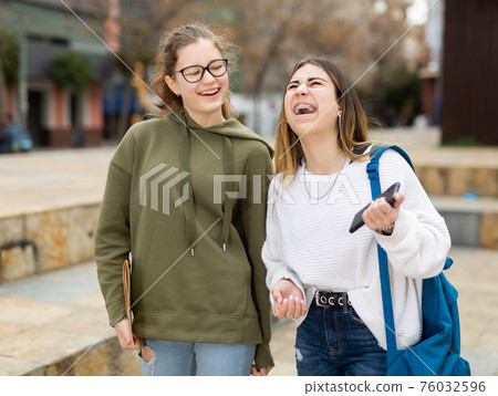 Two cheerful carefree female students walking down street Two cheerful carefree female students walking down street 76032596