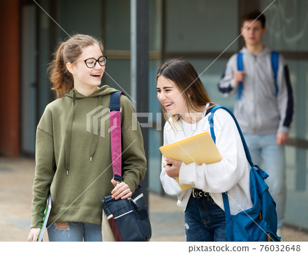 Two cheerful carefree female students walking down street Two cheerful carefree female students walking down street 76032648