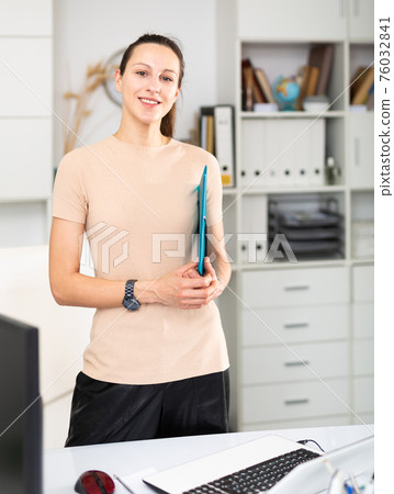 Positive girl secretary with folder for documents in office Positive girl secretary with folder for documents in office 76032841