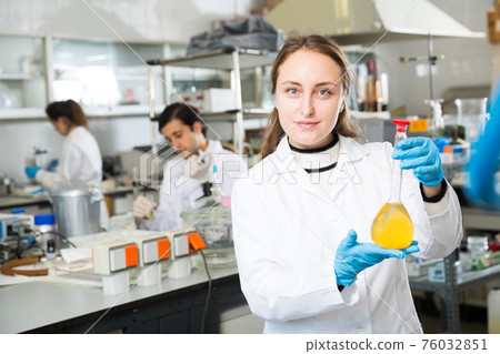 Female chemist analyzing liquid in test flasks Female chemist analyzing liquid in test flasks 76032851