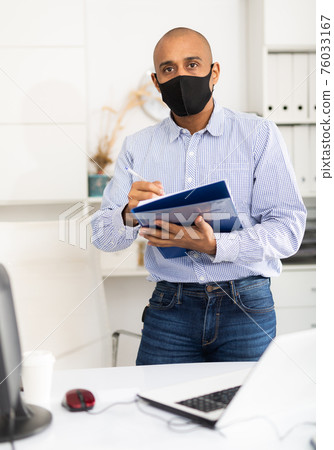 Portrait of positive business man in protective mask with folder of documents 76033167