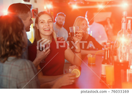 Smiling woman and man joying in the night club with drinks in the hand 76033169
