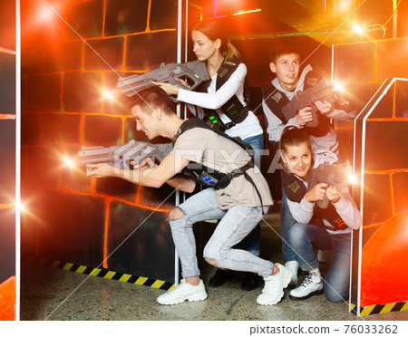 Ordinary Laser tag players young mens and womens playing in teams in dark laser tag station Ordinary Laser tag players young mens and womens playing in teams in dark laser tag station 76033262