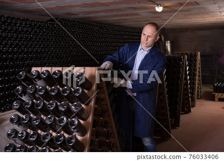 Male inspecting wine bottles in wine cellar 76033406