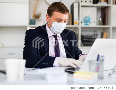 Entrepreneur in medical mask and gloves working in office 76033491