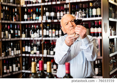 Older man inspecting quality of red wine in wine store in search of perfect wine for solemn occasion Older man inspecting quality of red wine in wine store in search of perfect wine for solemn occasion 76033559