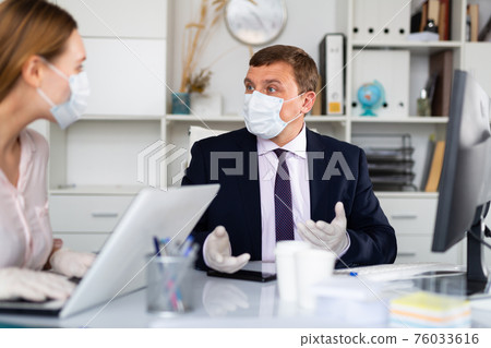 Entrepreneur in medical mask working with female coworker in office 76033616