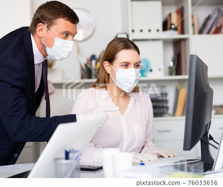 Businessman in face mask working with female assistant in office 76033656