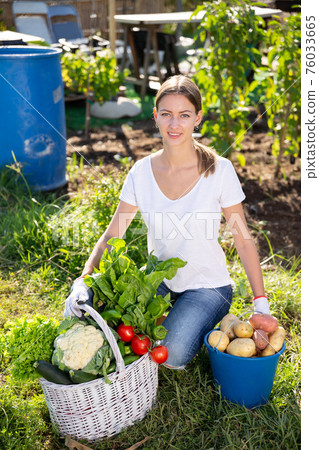 Girl farmer with basket and box of vegetables in the garden 76033665