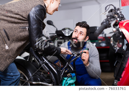 friendly male worker assisting female customer in repairing motorcycle in workshop friendly male worker assisting female customer in repairing motorcycle in workshop 76033761